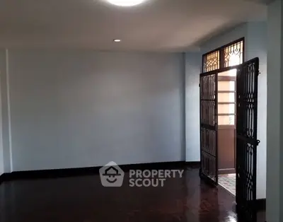 Spacious empty room with open door leading to balcony, featuring dark wooden floors and light walls.