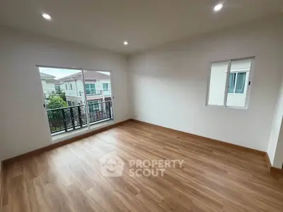 Spacious empty room with wooden flooring and large windows offering natural light and balcony access.