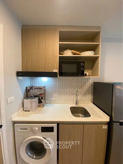 Modern compact kitchen with washing machine and microwave in a stylish apartment.