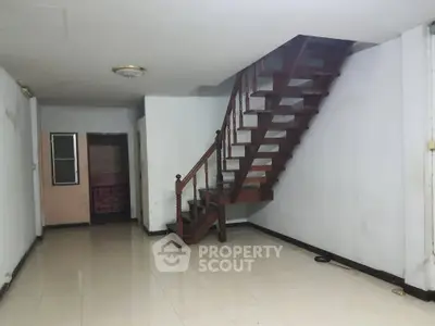 Spacious interior with wooden staircase and tiled flooring, ideal for renovation.