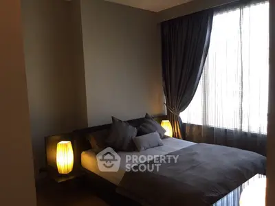 Cozy bedroom with elegant lighting and large window draped in dark curtains.