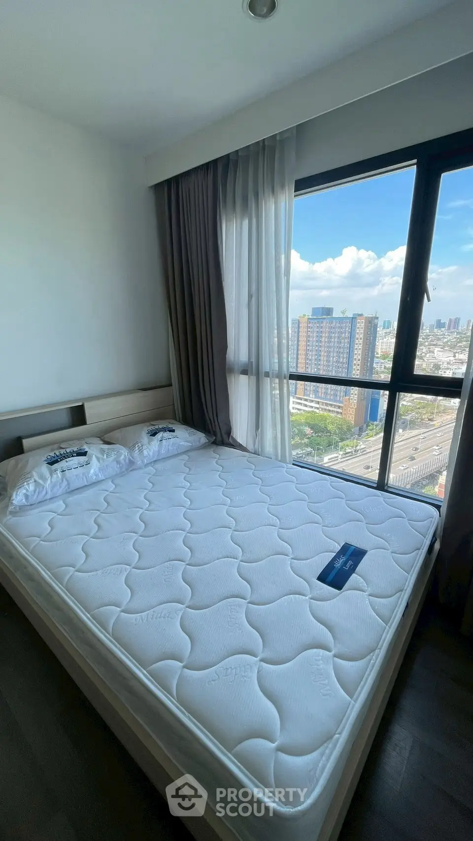 Spacious bedroom with large window offering stunning city views, featuring a comfortable bed and modern decor.
