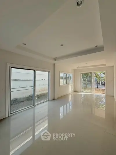 Spacious sunlit living room with large windows and glossy floors in modern home.