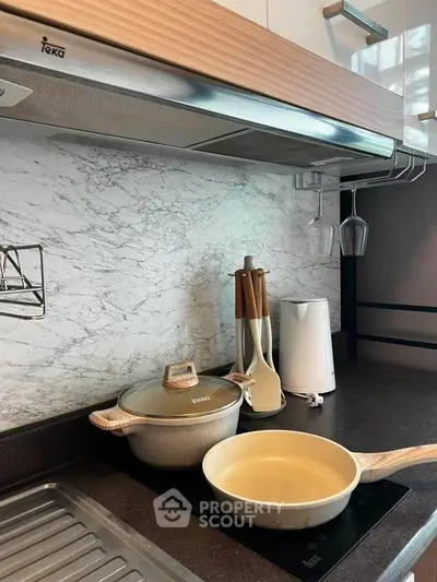Modern kitchen with sleek countertops and stylish cookware, featuring a Teka range hood and elegant marble backsplash.