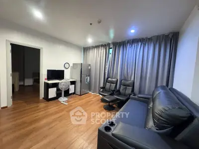 Modern living room with leather sofa, TV, and fridge, featuring wooden flooring and stylish curtains.
