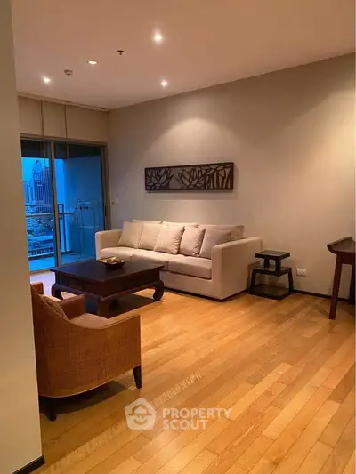 Elegant living room with wooden flooring and modern furniture, featuring a cozy sofa and city view balcony.