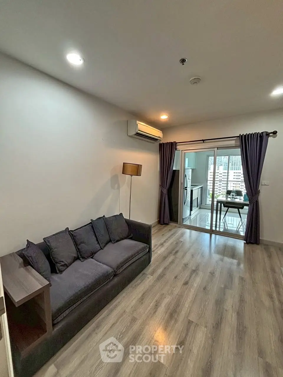 Modern living room with sleek flooring and cozy sofa, leading to a bright balcony with city views.