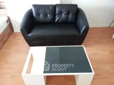 Modern living room with sleek black leather sofa and stylish glass-top coffee table on wooden floor.