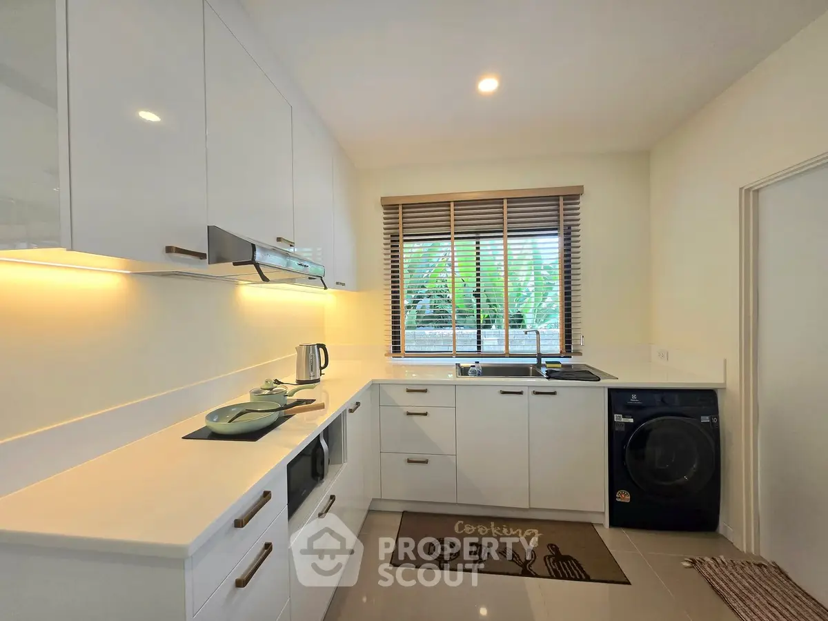 Modern kitchen with sleek white cabinets, built-in appliances, and a washing machine under natural light.