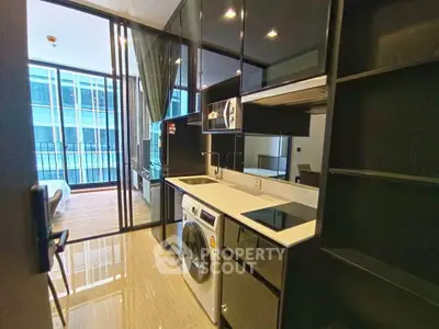 Modern kitchen with sleek appliances and open layout leading to a bright living area with balcony view.