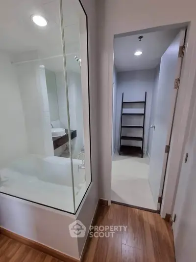 Modern bathroom with glass-enclosed bathtub and adjacent storage area in sleek apartment.