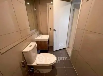 Modern bathroom with sleek fixtures and neutral tiles, featuring a toilet and compact sink.