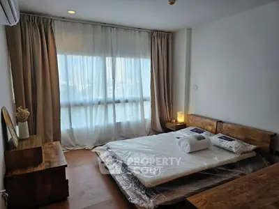Cozy bedroom with wooden furniture and large window with sheer curtains.