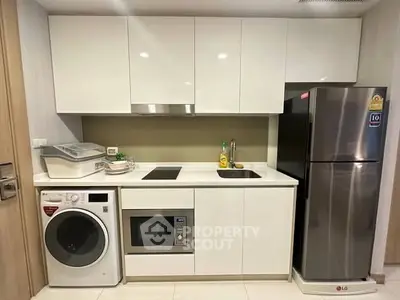 Modern kitchen with sleek white cabinets, washing machine, microwave, and stainless steel fridge.