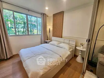 Cozy bedroom with large window and modern decor, offering serene views of lush greenery.