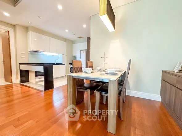 Modern dining area with wooden flooring and sleek kitchen design in open layout apartment.
