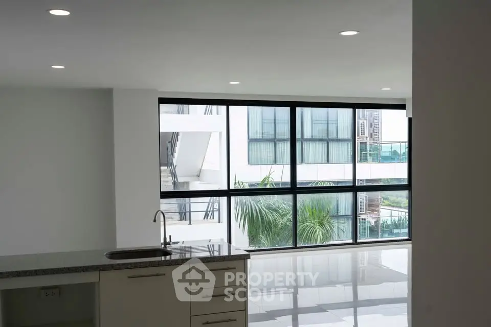 Spacious modern living room with large windows and sleek kitchen area, offering abundant natural light and urban views.