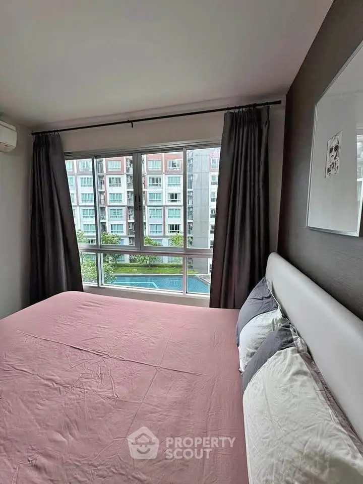 Cozy bedroom with large window offering a view of the pool and modern apartment buildings.