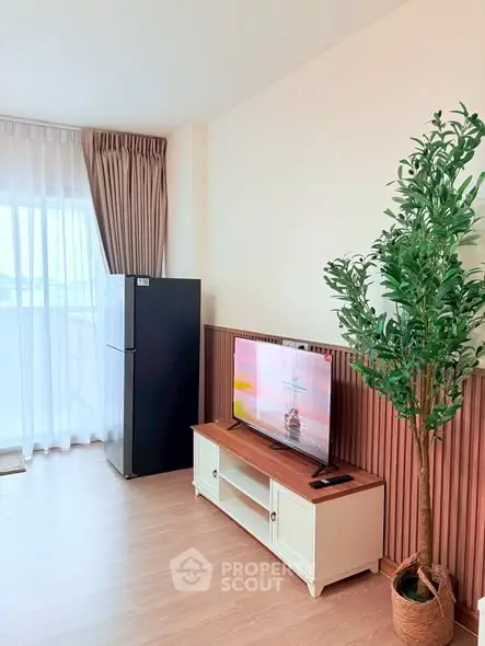 Modern living room with TV, fridge, and potted plant, featuring stylish decor and natural light.