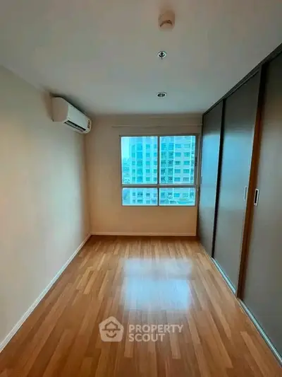 Spacious bedroom with wooden flooring and large window in modern apartment.