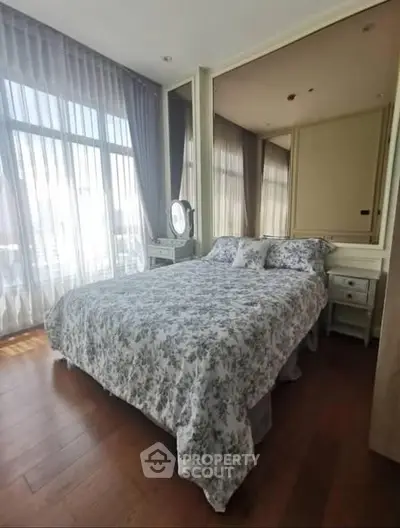 Elegant bedroom with floral bedding and large windows offering natural light.