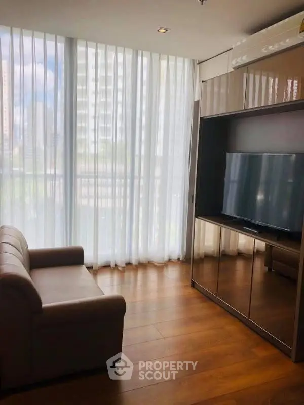 Modern living room with large TV and floor-to-ceiling windows in a high-rise apartment.