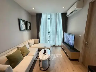 Modern living room with cozy sofa, large TV, and natural light from tall windows.