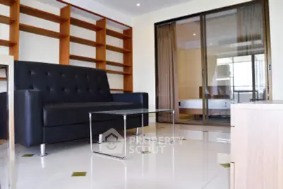 Modern living room with sleek black sofa and glass coffee table, featuring built-in wooden shelves.