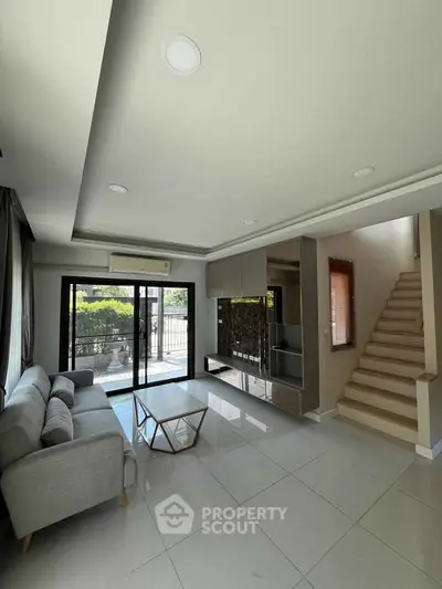 Modern living room with sleek design and staircase, featuring large windows and stylish furniture.