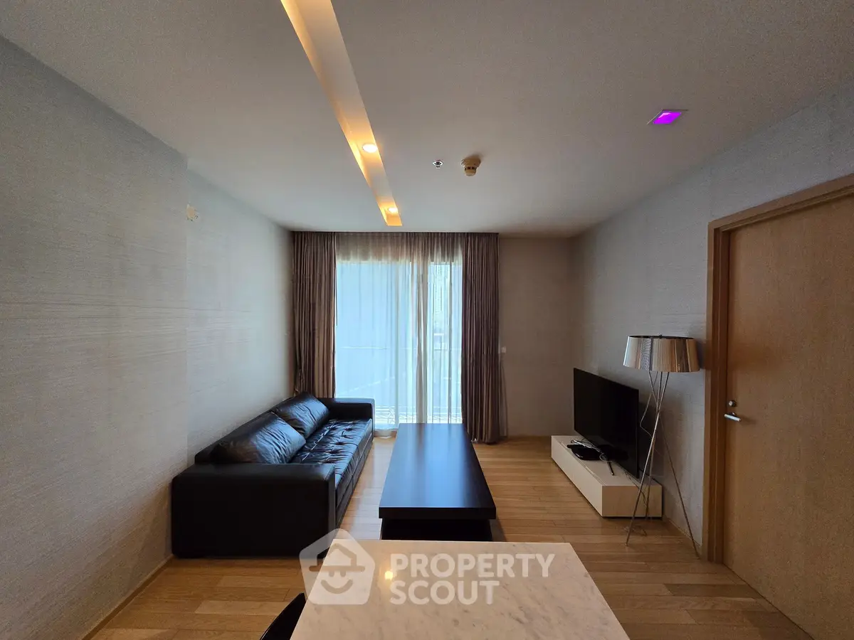 Modern living room with sleek furniture and natural light from large window.