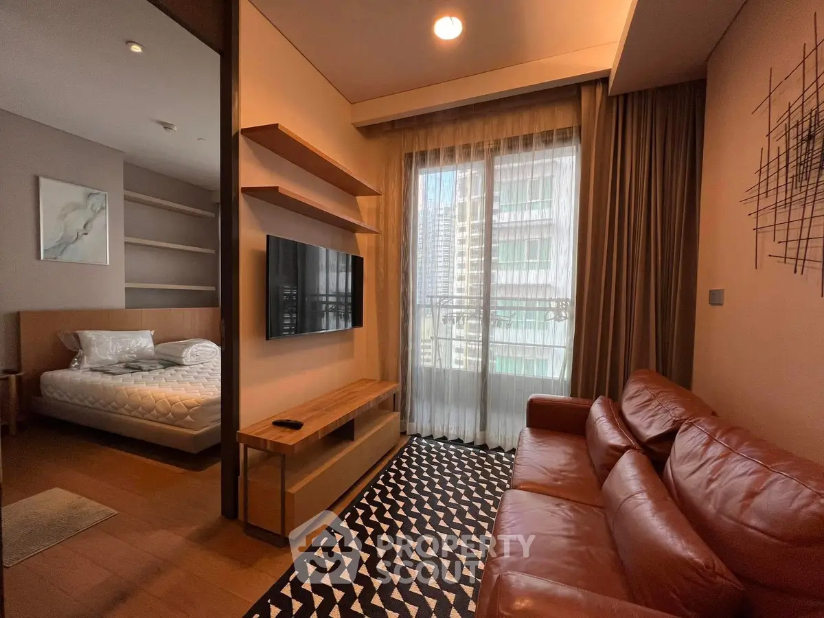 Modern living room with leather sofa and wall-mounted TV, adjacent to cozy bedroom.