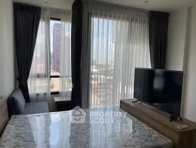 Modern bedroom with large windows and city view, featuring a TV and stylish curtains.