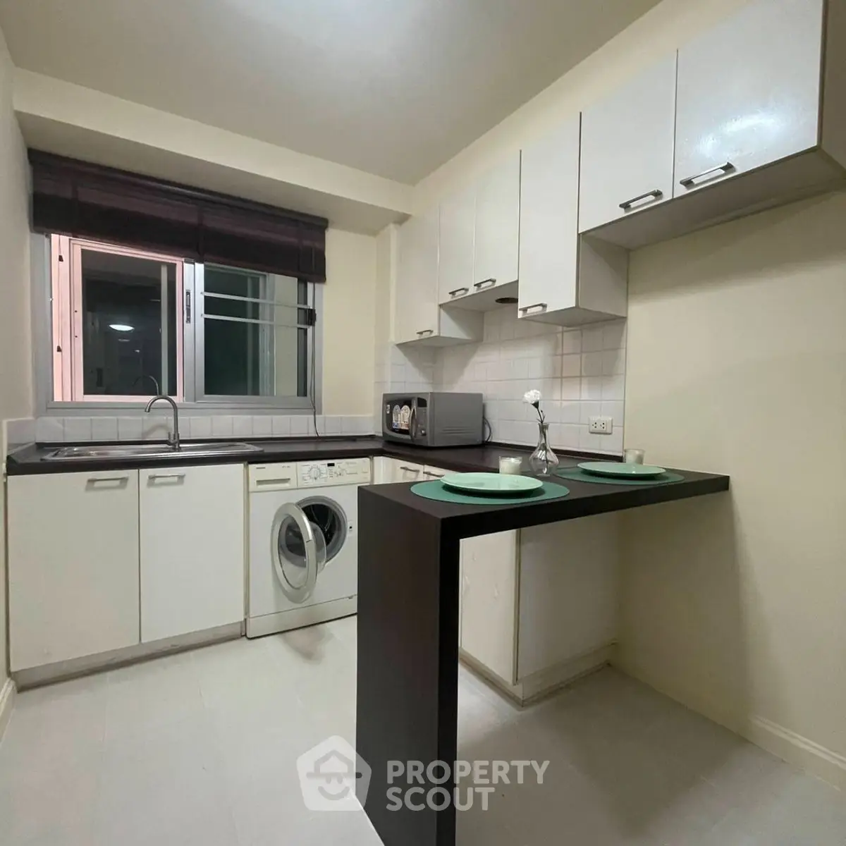 Modern kitchen with sleek white cabinets, washing machine, and breakfast bar in a cozy apartment.