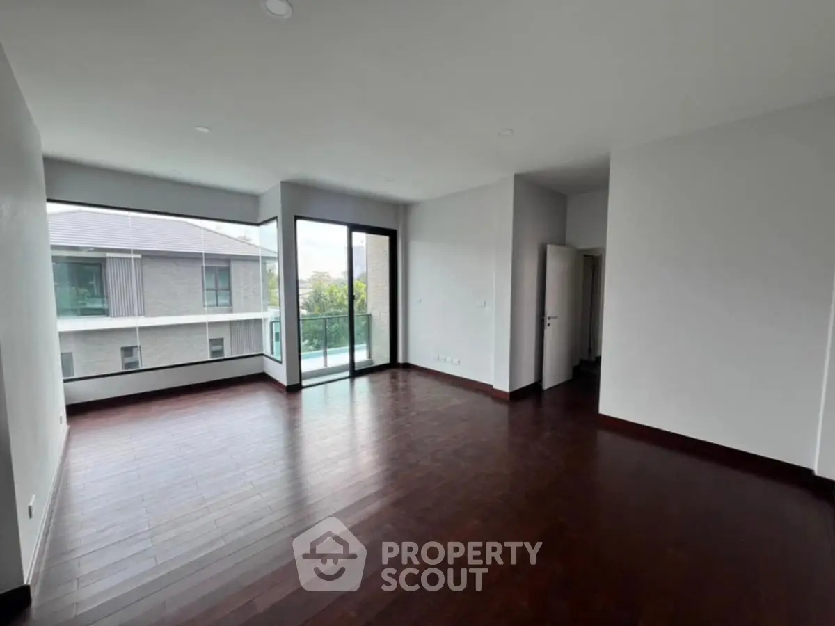 Spacious modern living room with dark wood flooring and large windows offering natural light.