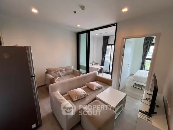 Modern living room with cozy seating and open view into bedroom