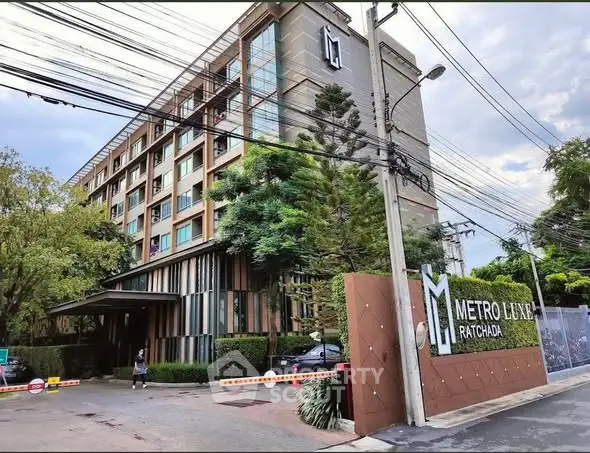 Modern apartment building with lush greenery at Metro Luxe Ratchada entrance.