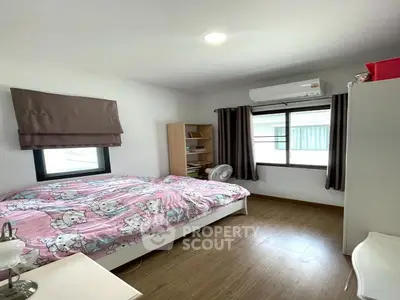 Cozy bedroom with wooden flooring, air conditioning, and ample natural light from two windows.