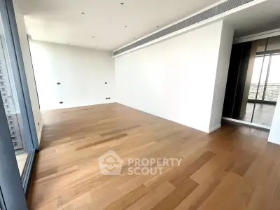 Spacious modern living room with wooden flooring and large windows offering natural light.