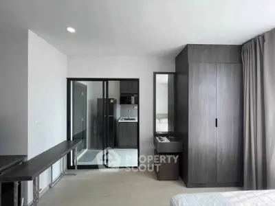 Modern bedroom with sleek wardrobe and glass partition leading to kitchen area.