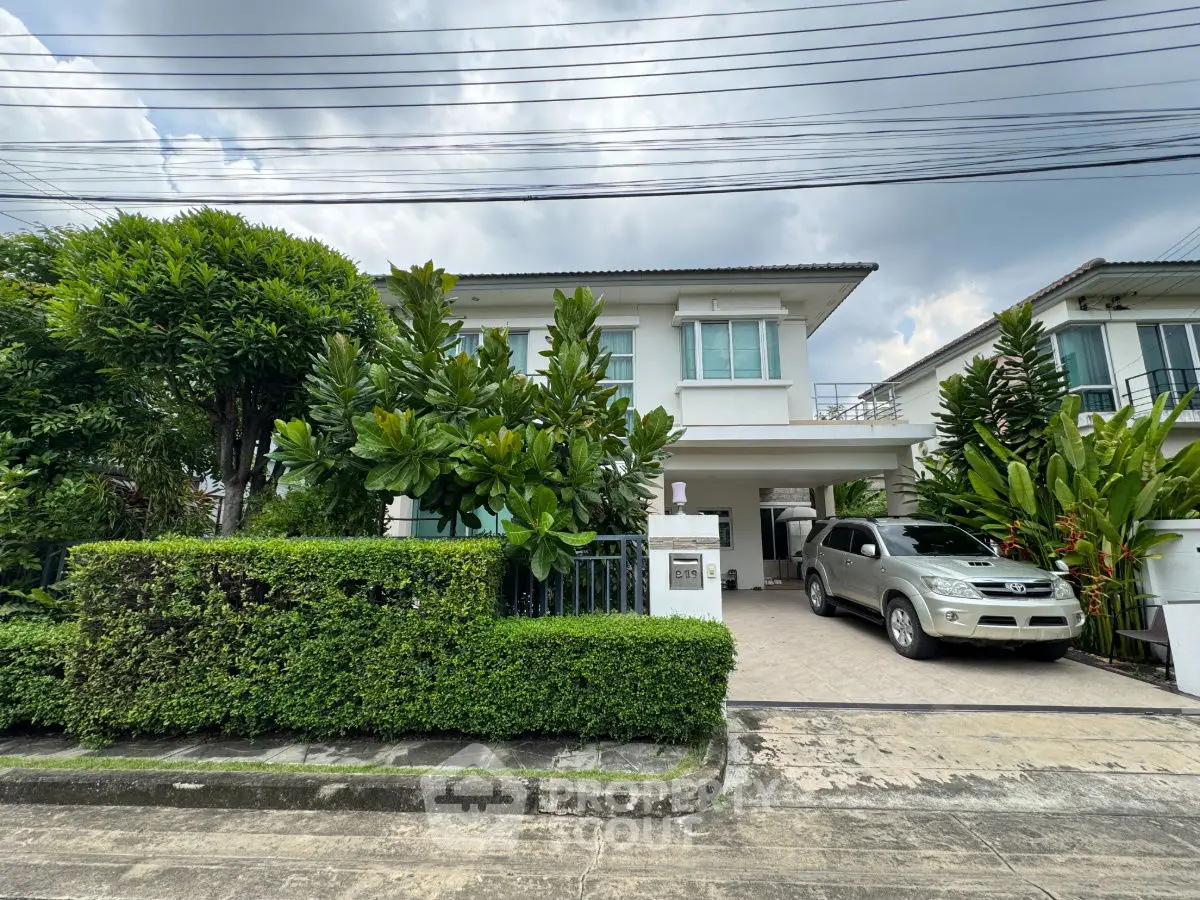 Charming two-story house with lush greenery and driveway in a serene neighborhood.