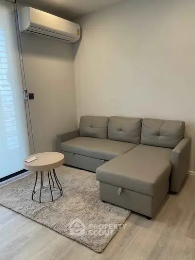 Modern living room with sleek gray sofa and stylish round coffee table on plush rug.
