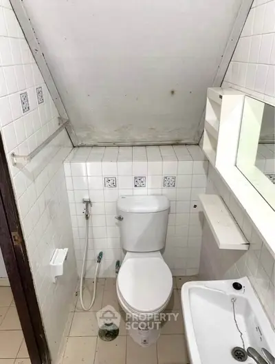 Compact bathroom with sloped ceiling and tiled walls, featuring a toilet and sink.