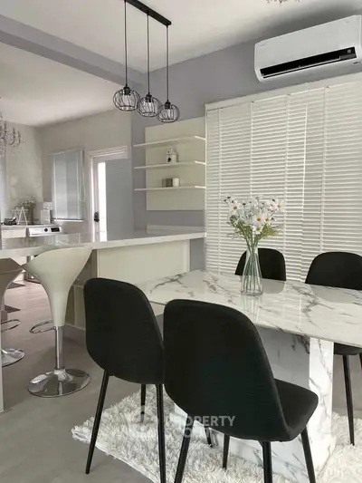 Modern kitchen with marble dining table and sleek black chairs, featuring open layout and stylish lighting.