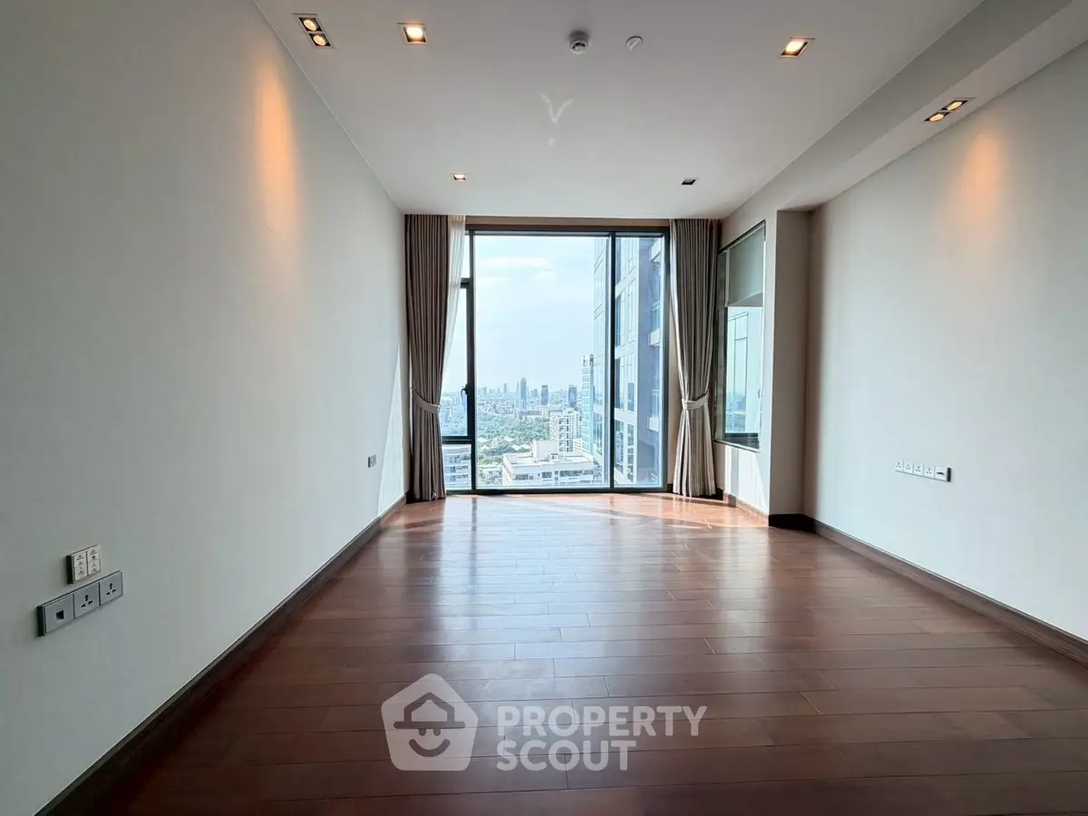 Spacious empty room with wooden flooring and city view through large windows.