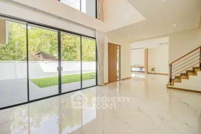 Spacious modern living room with large glass doors opening to a lush garden view.