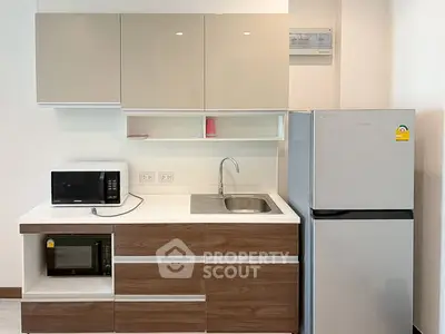 Modern kitchen with sleek cabinetry, microwave, and stainless steel fridge in a stylish apartment.