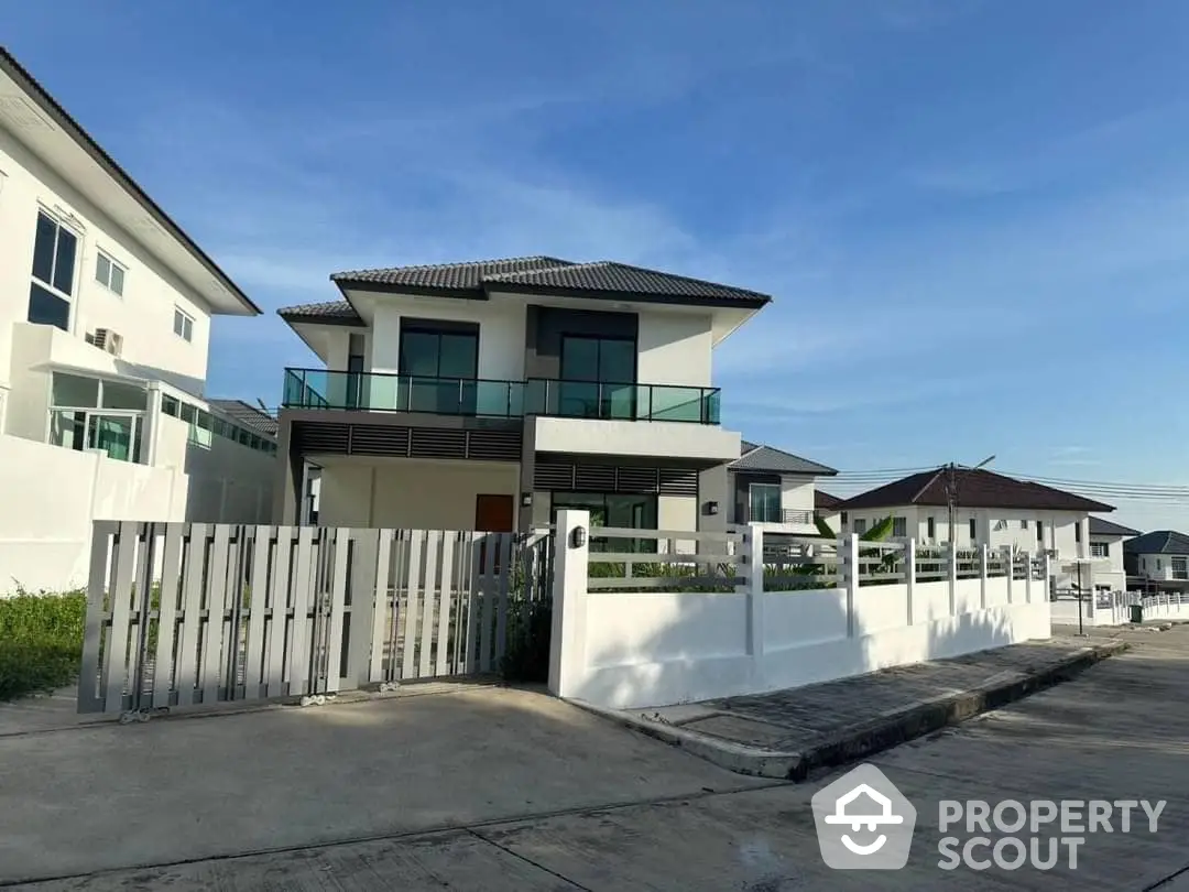 Spacious two-story modern home with large windows and a balcony, featuring a secure gated entrance and a paved driveway in a serene neighborhood.