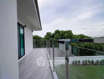 Spacious balcony with glass railing and lush green view in modern home.