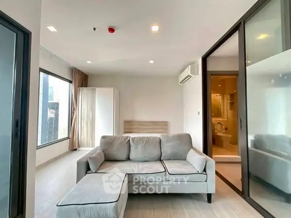 Modern living room with large windows and cozy gray sofa in high-rise apartment.