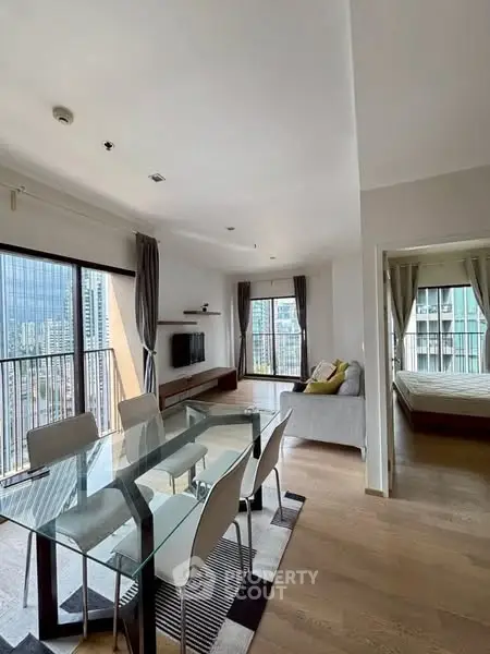 Modern open-plan living and dining area with city view, featuring glass table and cozy seating.